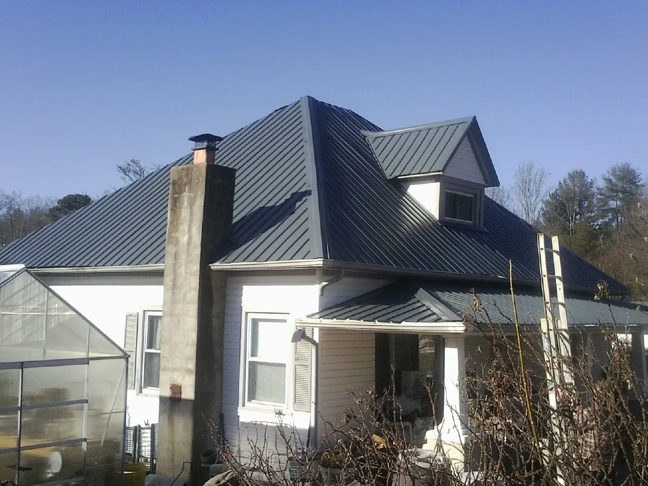 Dark blue standing seam metal roof on a white farmhouse with dormer — Slate & Tile Roof Repair by Roofing Brothers in Harrietta
