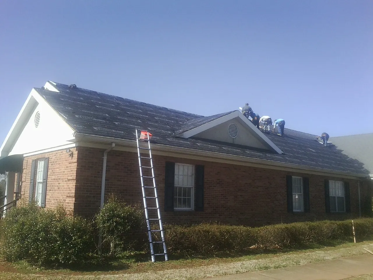 Crew tearing shingles off a brick ranch roof with a ladder set — Metal Roof Repair work by our crew in Harrietta