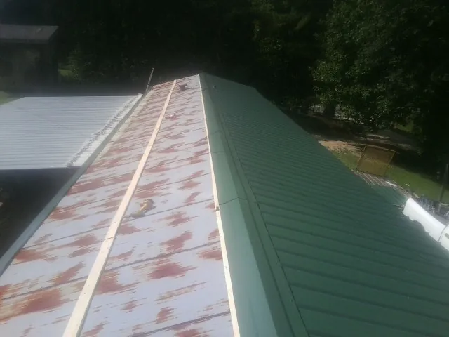 Old rusted panels beside newly installed green metal roofing — Wind Damage Roof Repair by Roofing Brothers in Harrietta