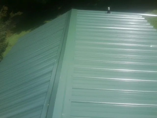 New green metal panels meeting at the ridge of a roof — Flat Roof Repair work by our crew in Harrietta