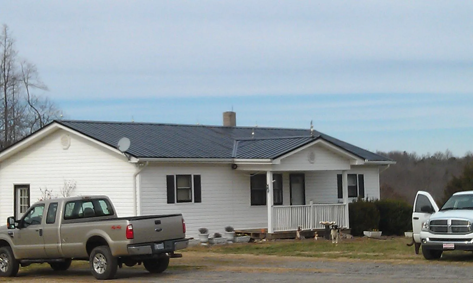 Finished dark metal roof on a white ranch home with work trucks parked in Harrietta