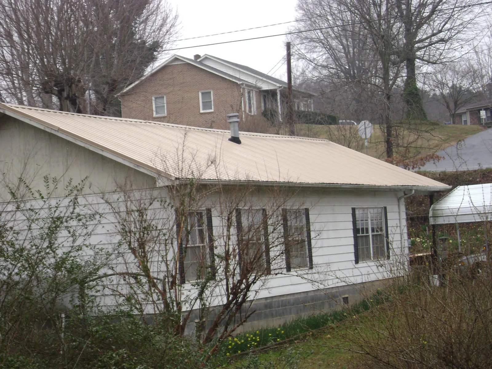Tan metal roof on a white sided house set into a hillside — Commercial Roofing by Roofing Brothers in Harrietta