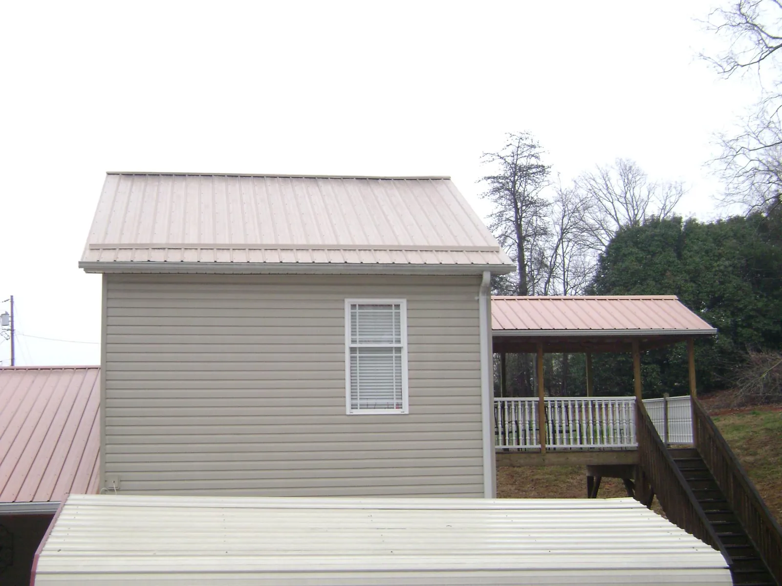 Tan metal roofs on a two story addition and attached porch, from a Roof Replacement job in Harrietta